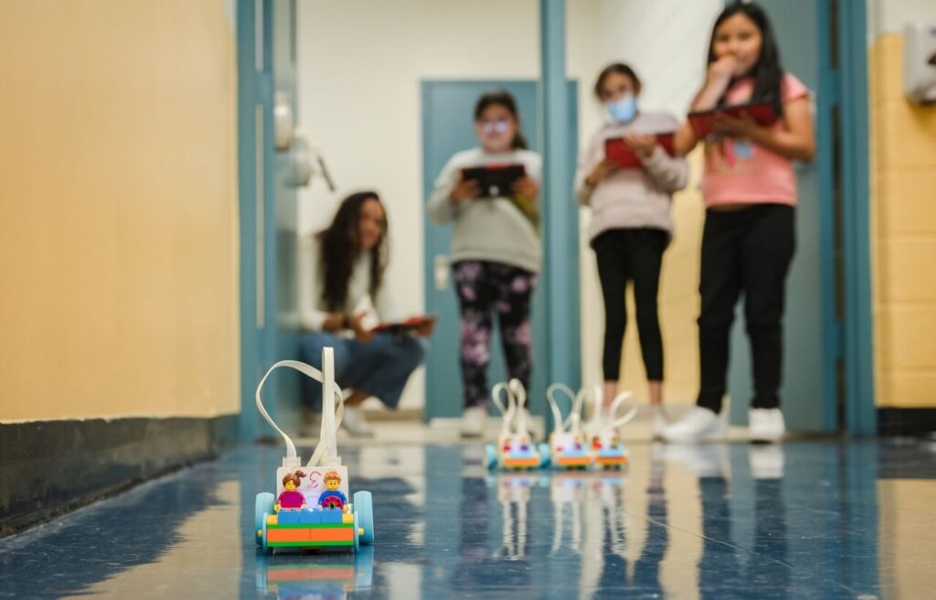 Students controlling remote lego cars in hall